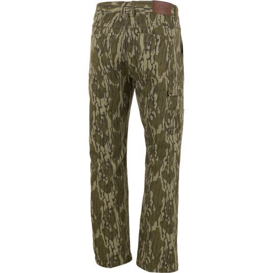 Back view of green and brown camouflage Throwback 80 Field Pant by Waterfowl in heavyweight cotton twill, with multiple pockets, straight legs, and a brown leather patch on the waistband.