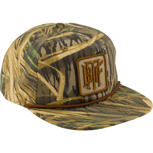The Drake x Lost Hat BMF Goat Rope Cap by Waterfowl features Mossy Oak Original Shadow Grass camo, a brown rope above the brim, and a square patch with stylized letters.