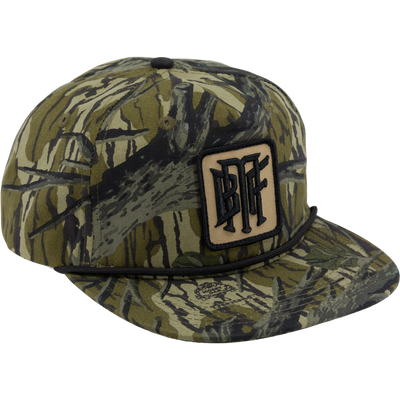 The Waterfowl Drake x Lost Hat BMF Goat Rope Cap in Mossy Oak Original Treestand features an adjustable snapback, black cord above the brim, and a front BFF patch, shown from a front-side angle.