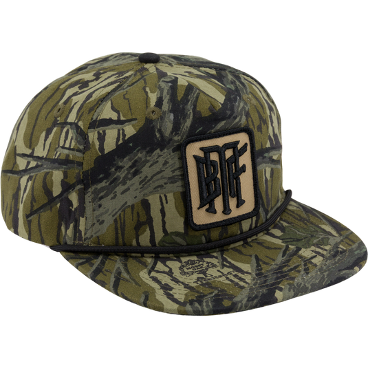 The Waterfowl Drake x Lost Hat BMF Goat Rope Cap in Mossy Oak Original Treestand features an adjustable snapback, black cord above the brim, and a front BFF patch, shown from a front-side angle.