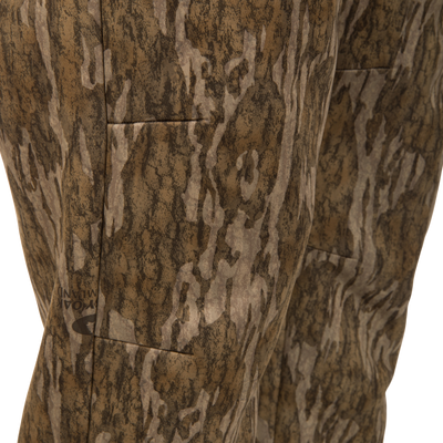 Close-up of brown and tan camouflage BMF Ultimate Wader Pants by Waterfowl, featuring a tree bark pattern, textured polyester fleece shell, visible stitching, and a faint logo on one leg.