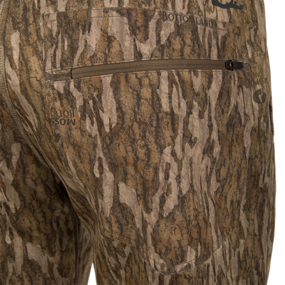 Close-up of BMF Ultimate Wader Pants by Waterfowl, featuring a brown and tan tree bark camo pattern with a horizontal back zipper pocket and subtle BOTTOMLAND and MOSSY OAK text.