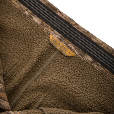 Close-up of the inside of BMF Ultimate Wader Pants from Waterfowl, showing brown fleece with camouflage trim, yellow L size tag, soft polyester shell, Sherpa lining, and black-gray stripe detail.