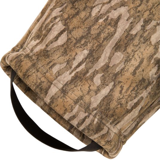 Close-up of brown and tan camouflage fabric with a black strap threaded through the hemmed edge of Waterfowl BMF Ultimate Wader Pants’ polyester fleece shell.