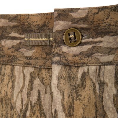 Close-up of the waistband of BMF Ultimate Wader Pants by Waterfowl, showing a brown button, belt loop, and a camouflage print in tan, brown, and green.