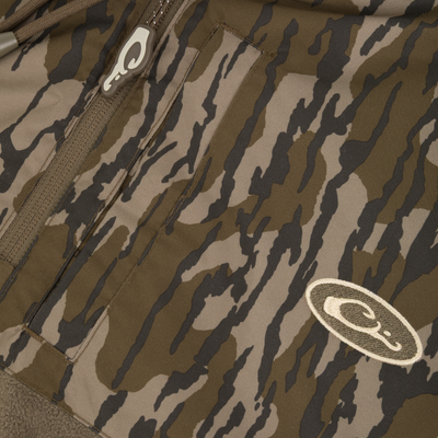Close-up of brown and green camouflage fabric with a zipper and two oval logos featuring white stylized text, resembling tiger stripes on the MST Quarter Zip Refuge Eqwader Jacket with Hood by Waterfowl.