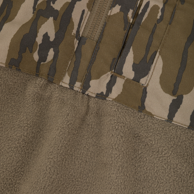 Close-up of fabric from a Waterfowl MST Quarter Zip Refuge Eqwader Jacket with Hood, showing camo on top and textured tan fleece below, joined by a visible seam.