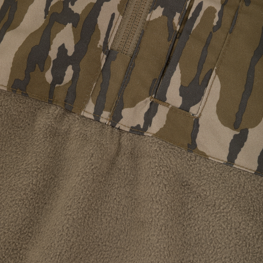 Close-up of fabric from a Waterfowl MST Quarter Zip Refuge Eqwader Jacket with Hood, showing camo on top and textured tan fleece below, joined by a visible seam.