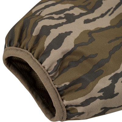 Close-up of the MST Quarter Zip Refuge Eqwader Jacket with Hood by Waterfowl, featuring a camouflage-patterned fabric sleeve with elastic edging in green, brown, and beige tiger stripe design.