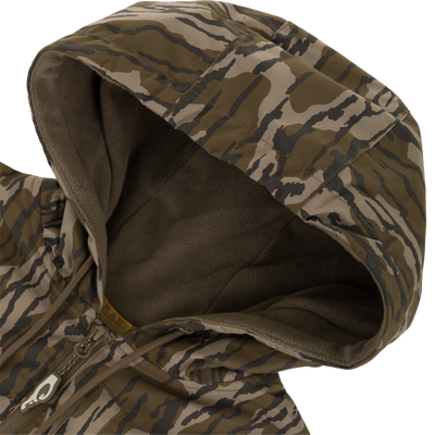 A close-up of the MST Quarter Zip Refuge Eqwader Jacket with Hood by Waterfowl, showing its green and brown camo pattern, quarter zip, and soft dark hood lining.