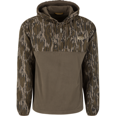 The Waterfowl MST Quarter Zip Refuge Eqwader Jacket with Hood features Mossy Oak Original Bottomland camo, a breathable design, drawstring hood, zippered chest pocket, embroidered logo, and solid olive green lower half.