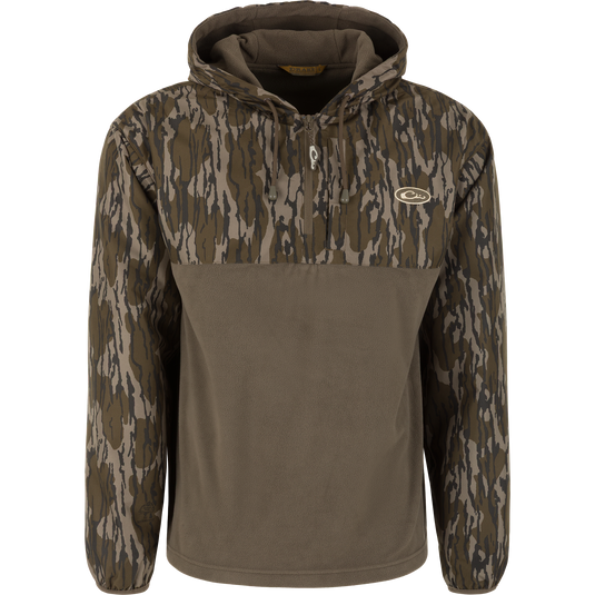 The Waterfowl MST Quarter Zip Refuge Eqwader Jacket with Hood features Mossy Oak Original Bottomland camo, a breathable design, drawstring hood, zippered chest pocket, embroidered logo, and solid olive green lower half.