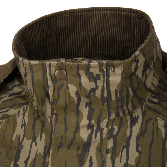 Close-up of an MST Drake Dry Waxed Cotton Wading Jacket in camouflage, featuring a high, dark green corduroy-lined collar and a snap-button closure.