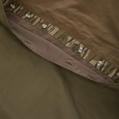 Close-up of a brown MST Drake Dry Waxed Cotton Wading Jacket showing the buttoned front placket with a camouflage interior trim.