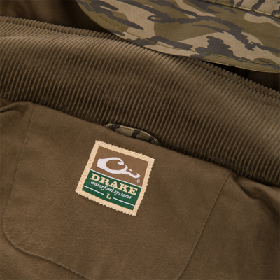 Close-up of the interior collar and label of a brown waxed cotton MST Drake Dry Waxed Cotton Wading Jacket by Waterfowl, showing the brand name and size large on a rectangular patch.