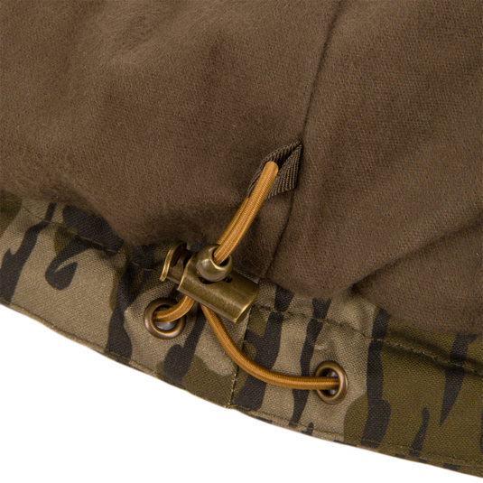 Close-up of the Waterfowl LST Insulated Waxed Cotton Vest in brown, with a camouflage trim, metal grommets, and a drawstring secured by a plastic cord lock.