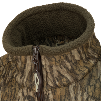 A close-up of the Waterfowl MST Hole Shot Two-Tone Eqwader Vest, featuring a camouflage pattern, high olive fleece-lined collar, and a brown zipper for cozy, sherpa-like warmth.