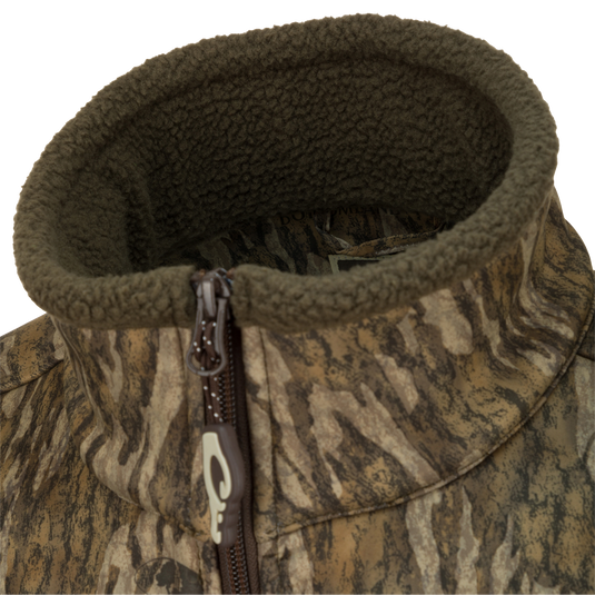 A close-up of the Waterfowl MST Hole Shot Two-Tone Eqwader Vest, featuring a camouflage pattern, high olive fleece-lined collar, and a brown zipper for cozy, sherpa-like warmth.
