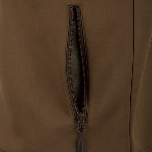 A close-up of the Waterfowl MST Hole Shot Two-Tone Eqwader Vest in brown, featuring a windproof design and a partially open vertical zippered pocket revealing the interior.