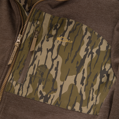 MST Heritage Hybrid Windproof Jacket with camo pocket, tan Drake zipper, and embroidered logo. Features water-resistant shell and fleece lining for hunting durability.