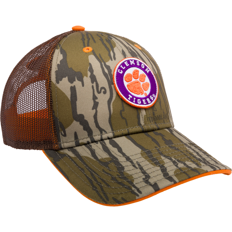 Clemson Bottomland Mesh Back Cap with Mossy Oak Camo pattern. Structured trucker cap with embroidered college logo, mesh panels, and snap-back closure. Ideal for hunting and outdoor enthusiasts.