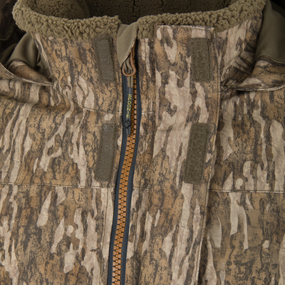 Close-up of a camouflage Spoonie Shoveler Insulated Jacket featuring a fleece-lined collar and a front zipper with a logo on the pull tab.