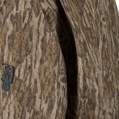Close-up of a brown camouflage Spoonie Waterproof Fleece Lined Quarter Zip Jacket with a vertical pocket opening and an embroidered patch featuring a black cat icon and yellow text on the sleeve.