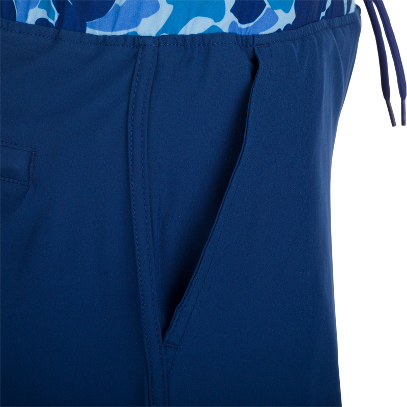 A close-up of the Youth Commando Lined Volley Short 5, a versatile blue and white fabric short with a scalloped hem, elastic waistband, and adjustable drawstring. Features include quick-drying, moisture-wicking, and a built-in interior comfort liner.