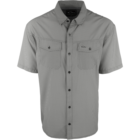 A close-up of the Traveler's Check Shirt S/S, a black and white shirt with collar and button details. Made with a lightweight, breathable poly/spandex fabric for ultimate comfort and freedom of movement. Ideal for the man on the go, whether on vacation or running errands. Moisture-wicking and wrinkle-resistant. 2 chest pockets with button flaps.