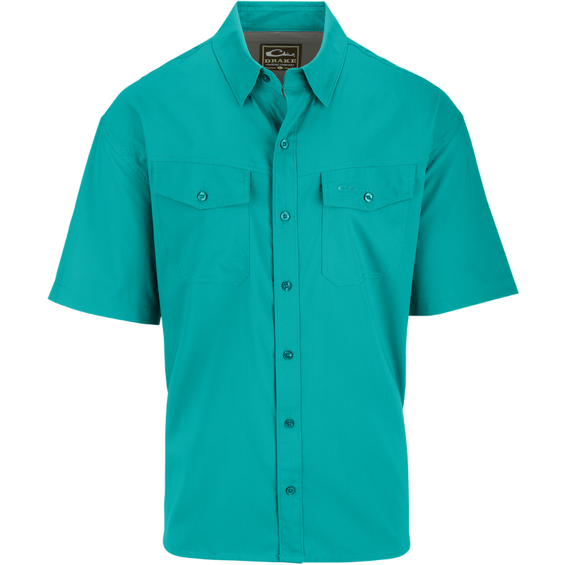A close-up of the Traveler's Solid Dobby Shirt S/S, featuring a hidden button-down collar, two chest pockets with button-through flaps, and a split tail hem. Constructed with 100% Polyester textured dobby fabric, this shirt is featherweight at 79 GSM, moisture-wicking, and quick-drying. It also offers UPF30 sun protection. Versatile for any occasion, this shirt is perfect for seasons to come.