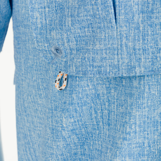 A close-up of the Heritage Heather Shirt S/S, a blue short sleeve shirt made of 100% polyester micro mesh. Features include UPF30 sun protection, moisture-wicking, and a hidden button-down collar. Perfect for outdoor activities or office wear.